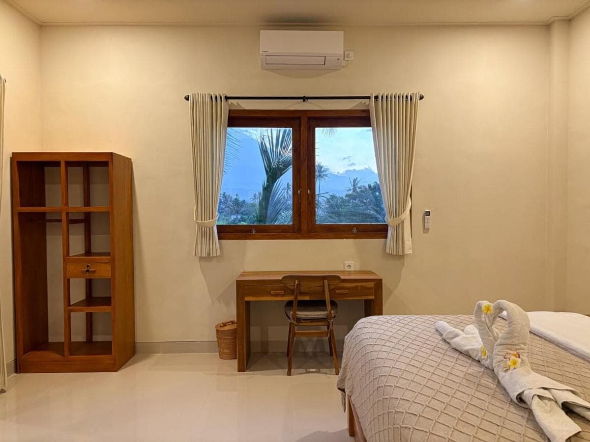 a bedroom with a bed and a desk and a window at Kayana Amed in Amed