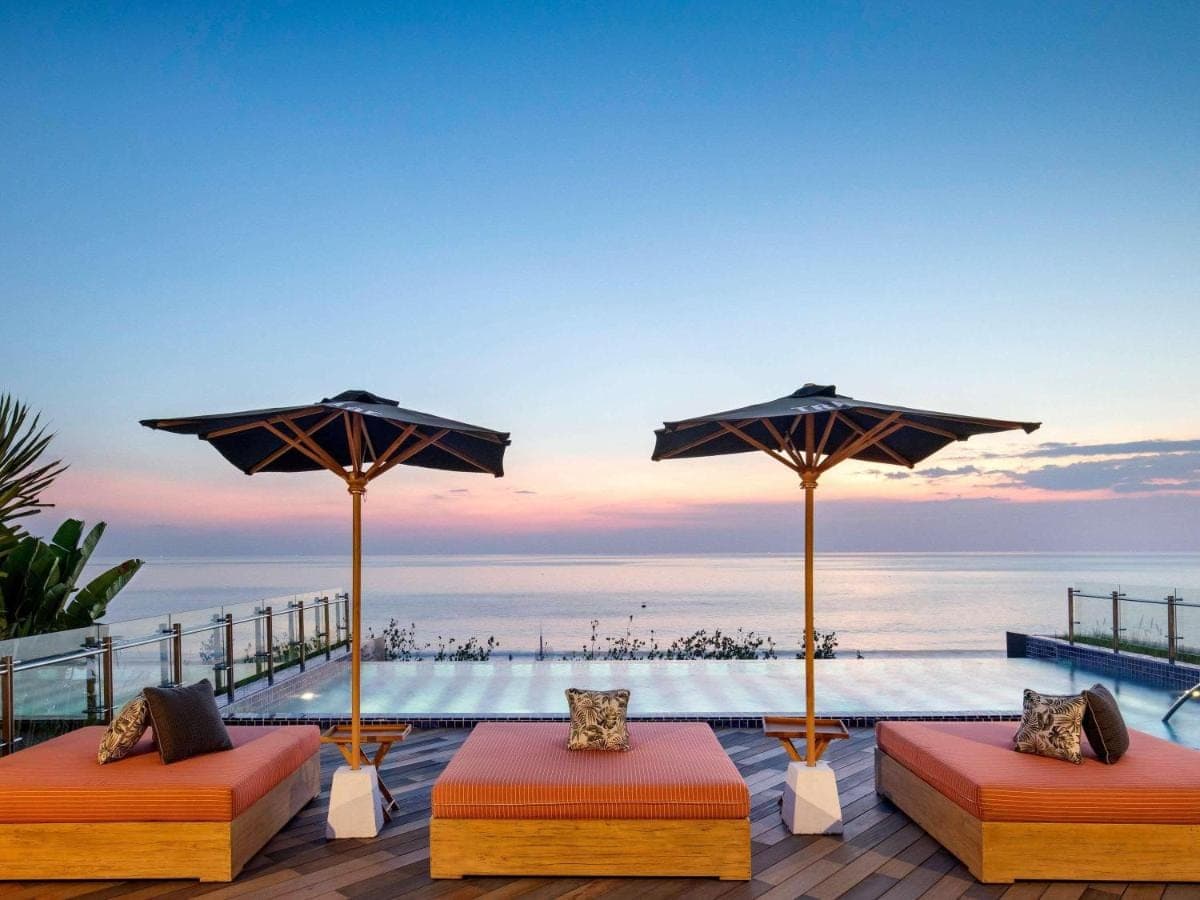 a deck with two beds and umbrellas and the ocean at Tribe Bali Kuta Beach in Kuta