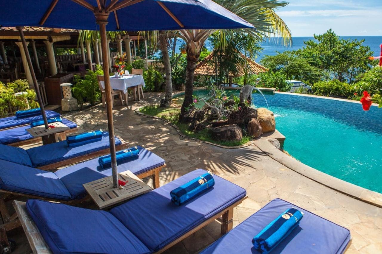 an outdoor pool with blue lounge chairs and an umbrella at Blue Moon Villas Resort in Amed