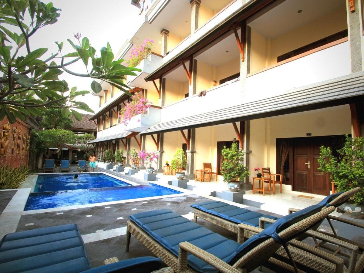 a resort with a swimming pool and chairs and a building at Jesens Inn II in Kuta