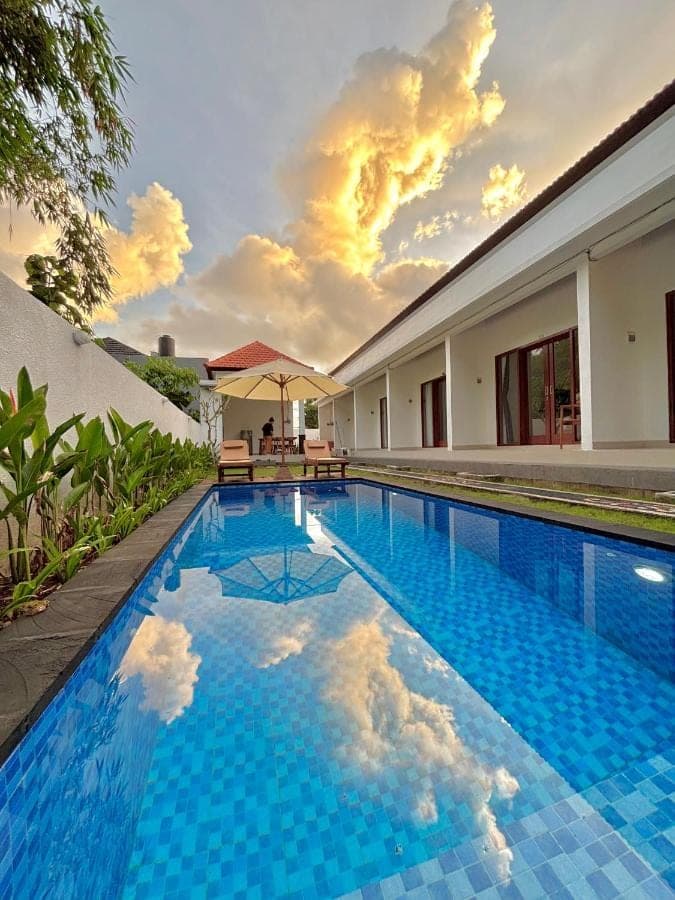 a swimming pool with blue tiles in front of a house at Amitha Lodge Uluwatu in Uluwatu