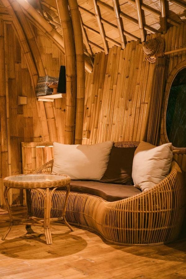 a rattan couch in a room with a table at Arcada Bali Bamboo House in Sidemen