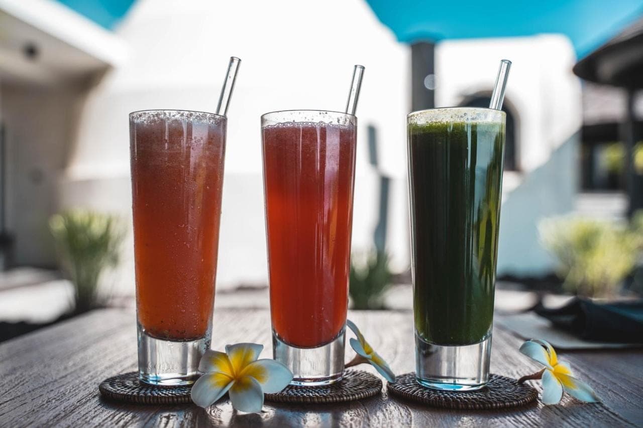three drinks are sitting on a wooden table at The Istana in Uluwatu
