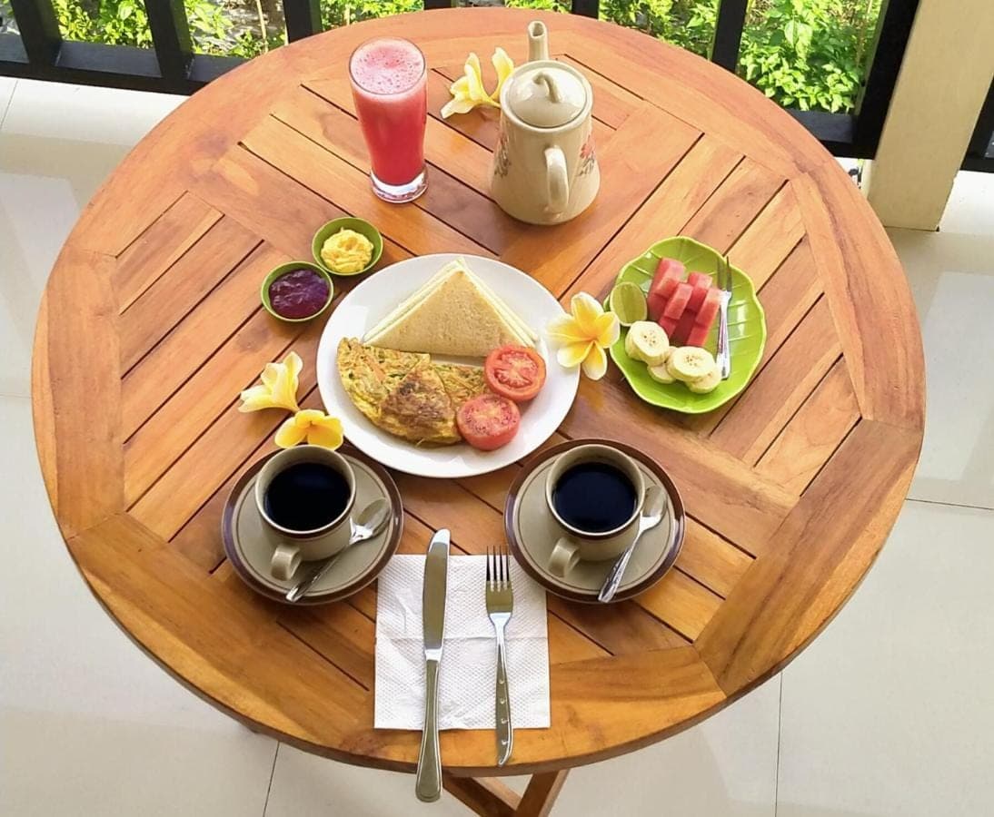 a wooden table with a plate of breakfast food on it at Mantra Guesthouse Sidemen in Sidemen
