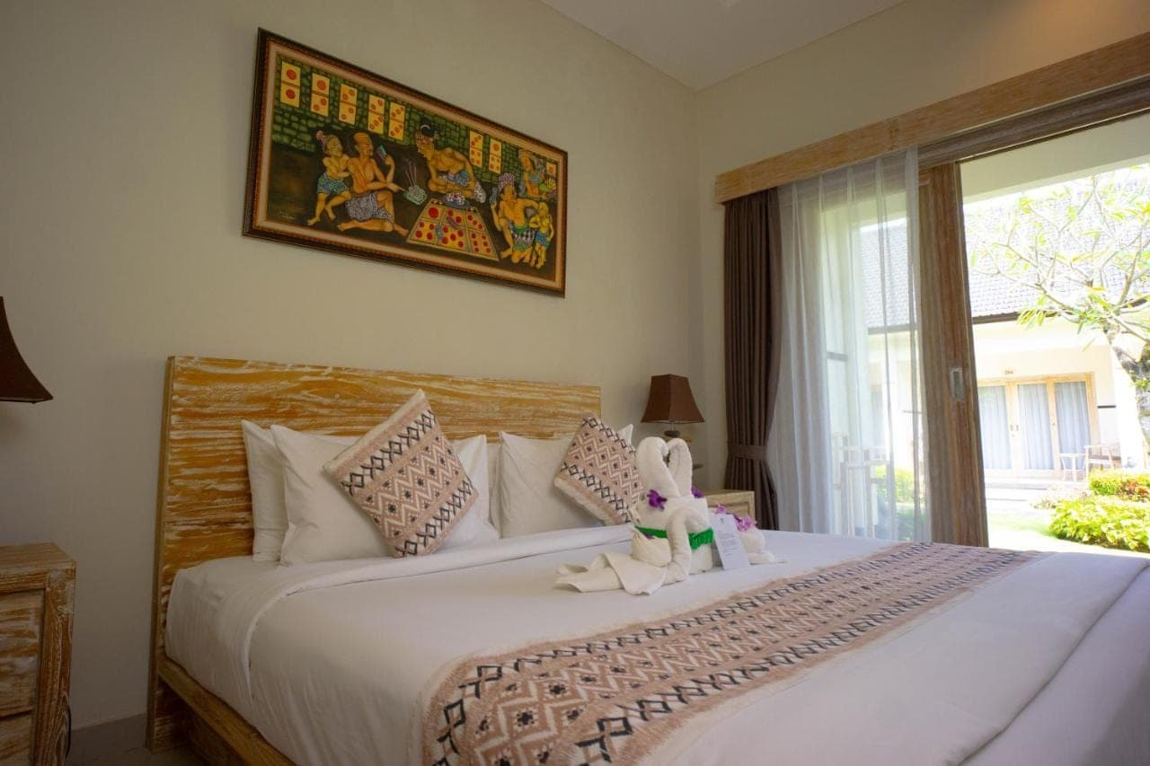 a bedroom with a large white bed with a window at Green D'mel Bali in Nusa Dua
