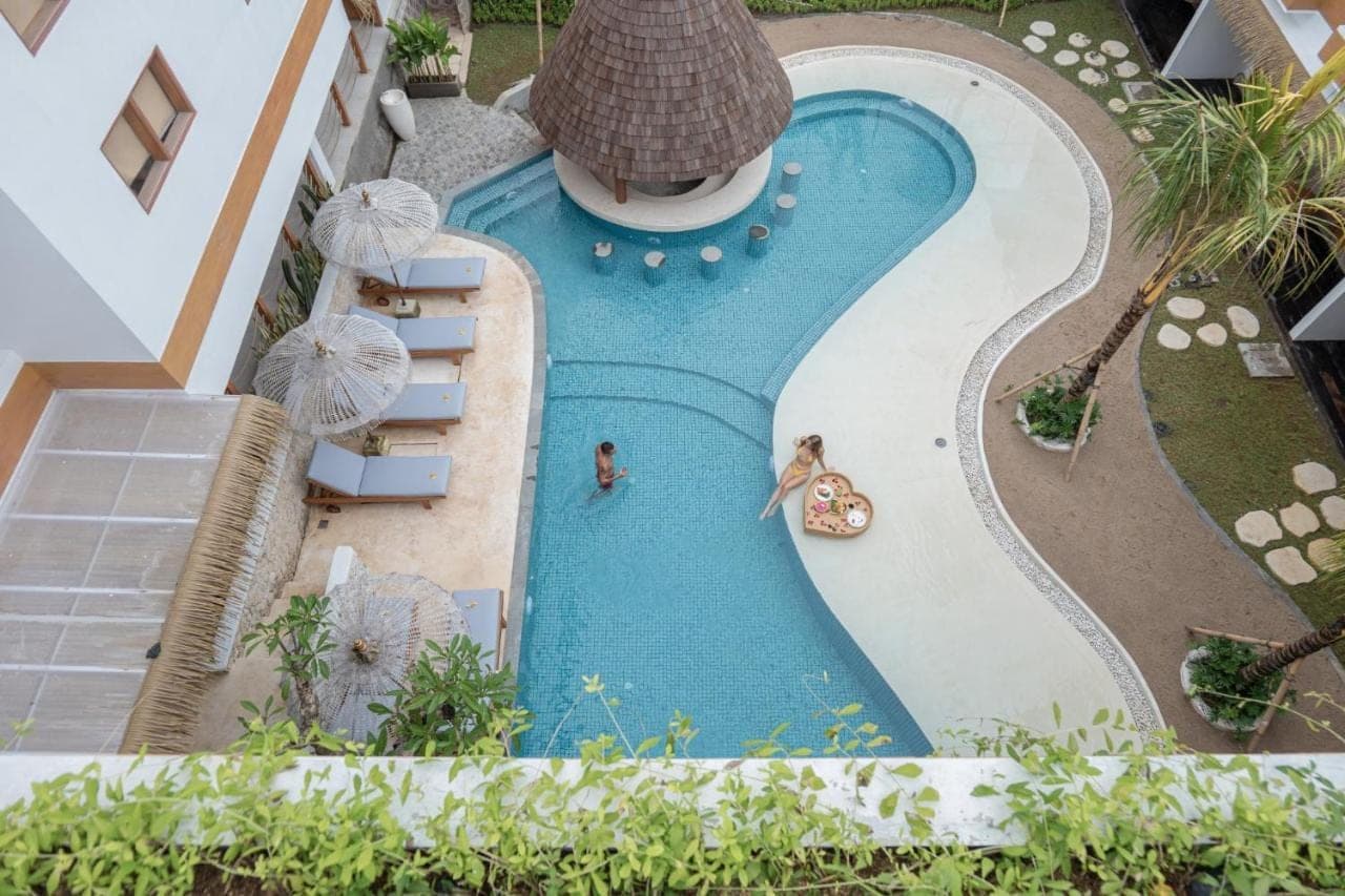 an overhead view of a swimming pool with two people and umbrellas at Roomates Beach Hostel Canggu by Ini Vie Hospitality in Canggu