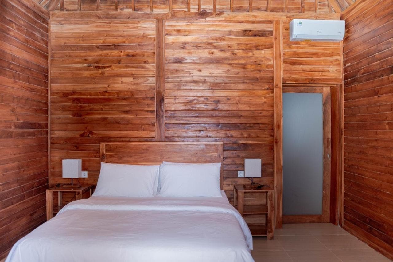 a bed in a room with a wooden wall at Kasturi Uluwatu in Uluwatu