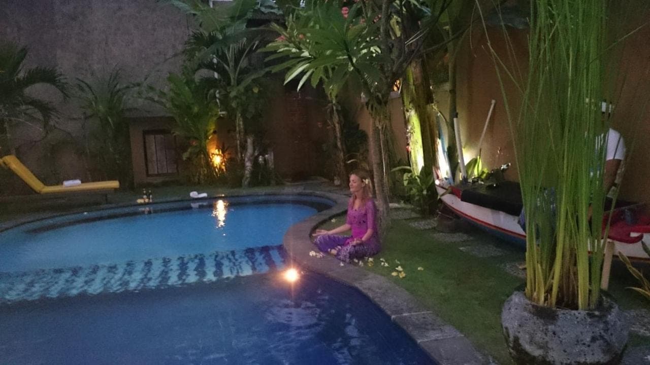 a woman sitting on the grass next to a swimming pool at Praschita Bali in Sanur