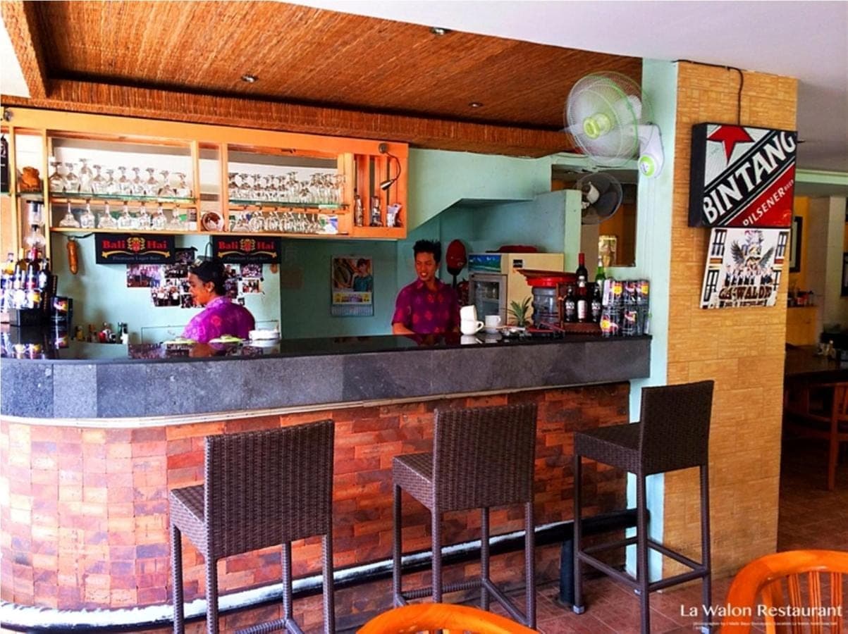 two men standing at a bar in a restaurant at La Walon Hotel in Kuta