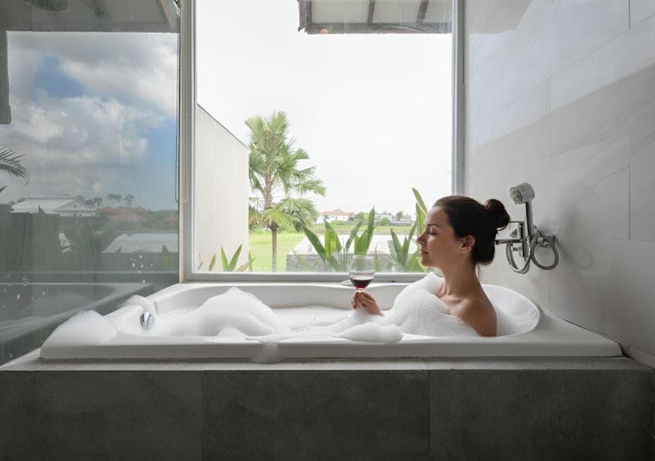 a woman sitting in a bath tub with a glass of wine at The Wina Villa Seminyak, Near Potato Head Beach Club in Seminyak