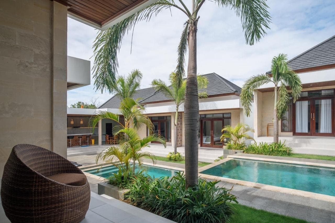 an exterior view of a villa with a swimming pool and palm trees at JANARA Uluwatu Villa in Uluwatu