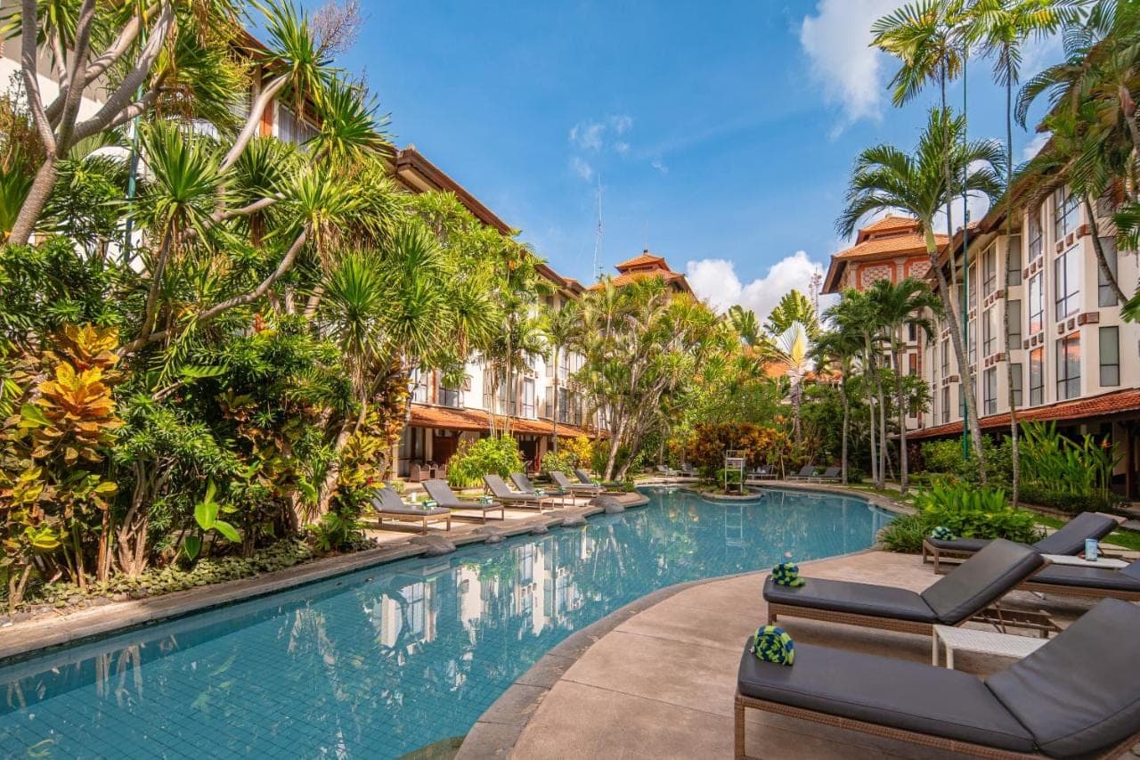 a pool at a resort with lounge chairs and palm trees at Prime Plaza Hotel Sanur \u2013 Bali in Sanur