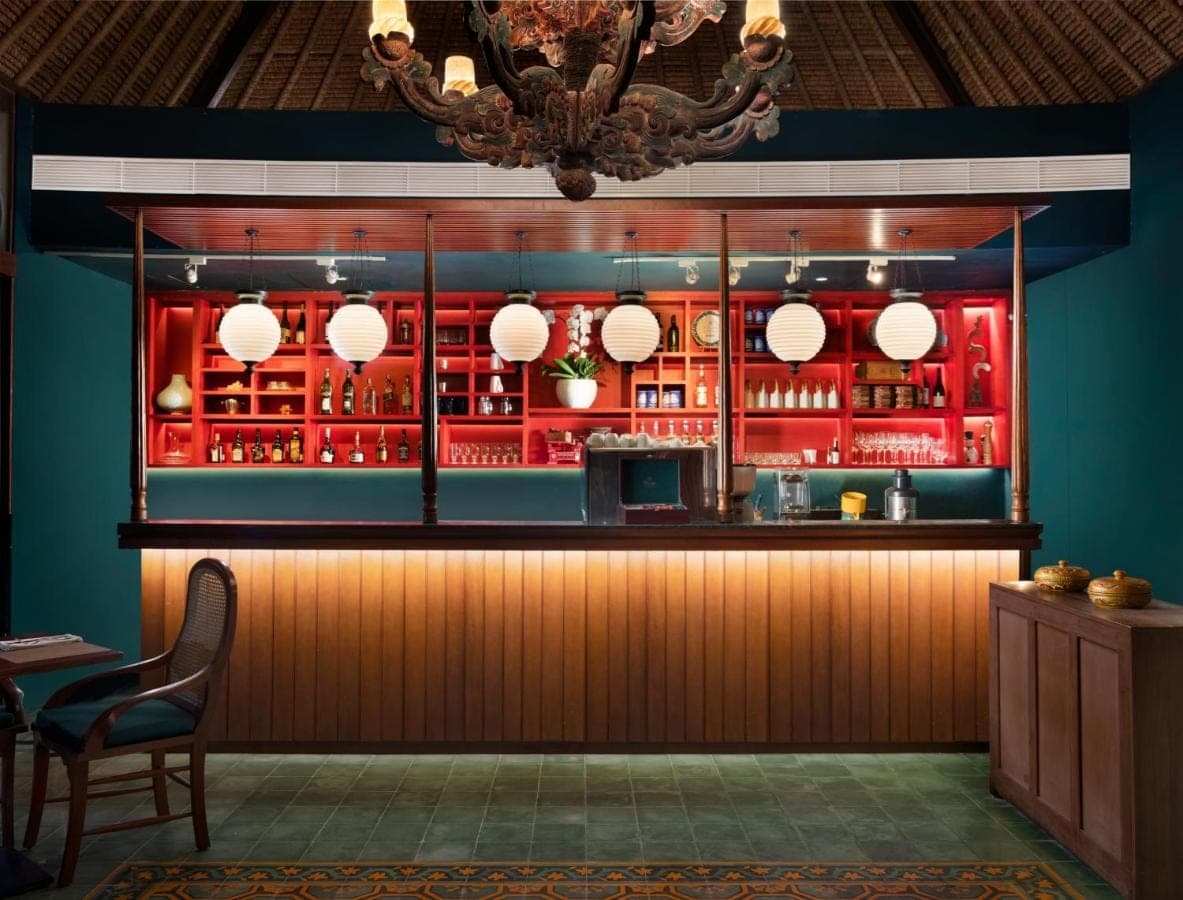 a restaurant with a bar with red cabinets and a chandelier at Sudamala Resort, Sanur, Bali in Sanur
