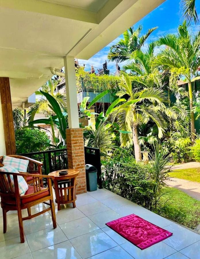 a porch with a table and chairs and palm trees at Sama Sama Amed in Amed