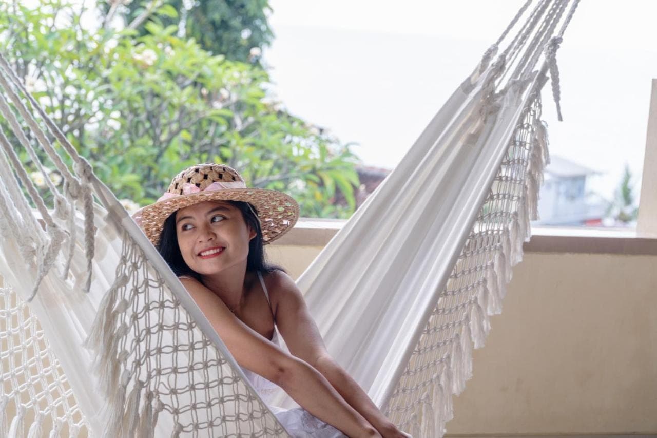 a woman in a straw hat sitting in a hammock at Amed Cafe & Hotel Kebun Wayan in Amed