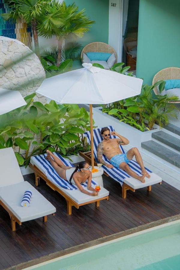 two people laying on chairs under an umbrella at Lomo Boutique Hotel & Villas, Uluwatu in Uluwatu