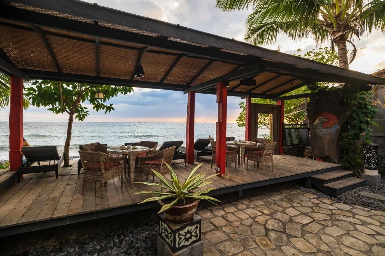 a wooden deck with tables and chairs on the beach at Amed Lodge by Sudamala Resorts in Amed
