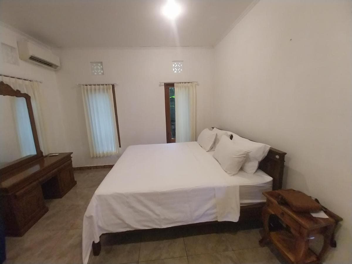 a bedroom with a white bed and a wooden table at D,Jajang Guest House in Nusa Dua