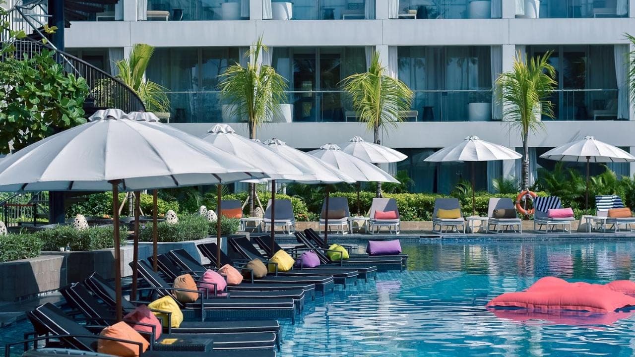 a pool with chaise lounges and umbrellas next to a building at The Stones Hotel - Legian Bali in Kuta