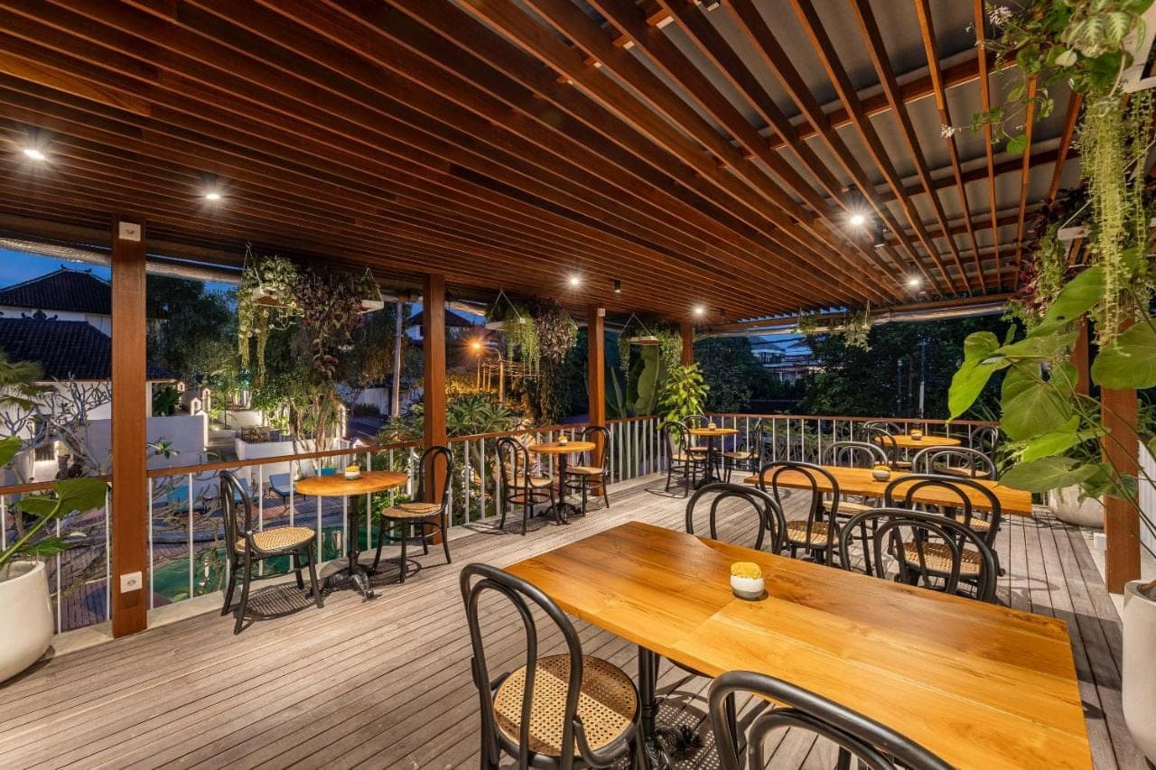 a patio with tables and chairs on a deck at Ecozy Dijiwa Canggu in Canggu