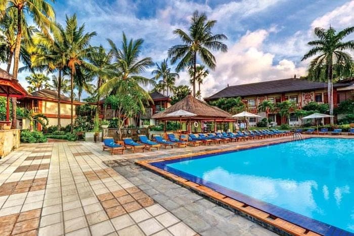 a resort swimming pool with chairs and palm trees at Private Apartment 6505 at the Jayakarta Residence in Seminyak