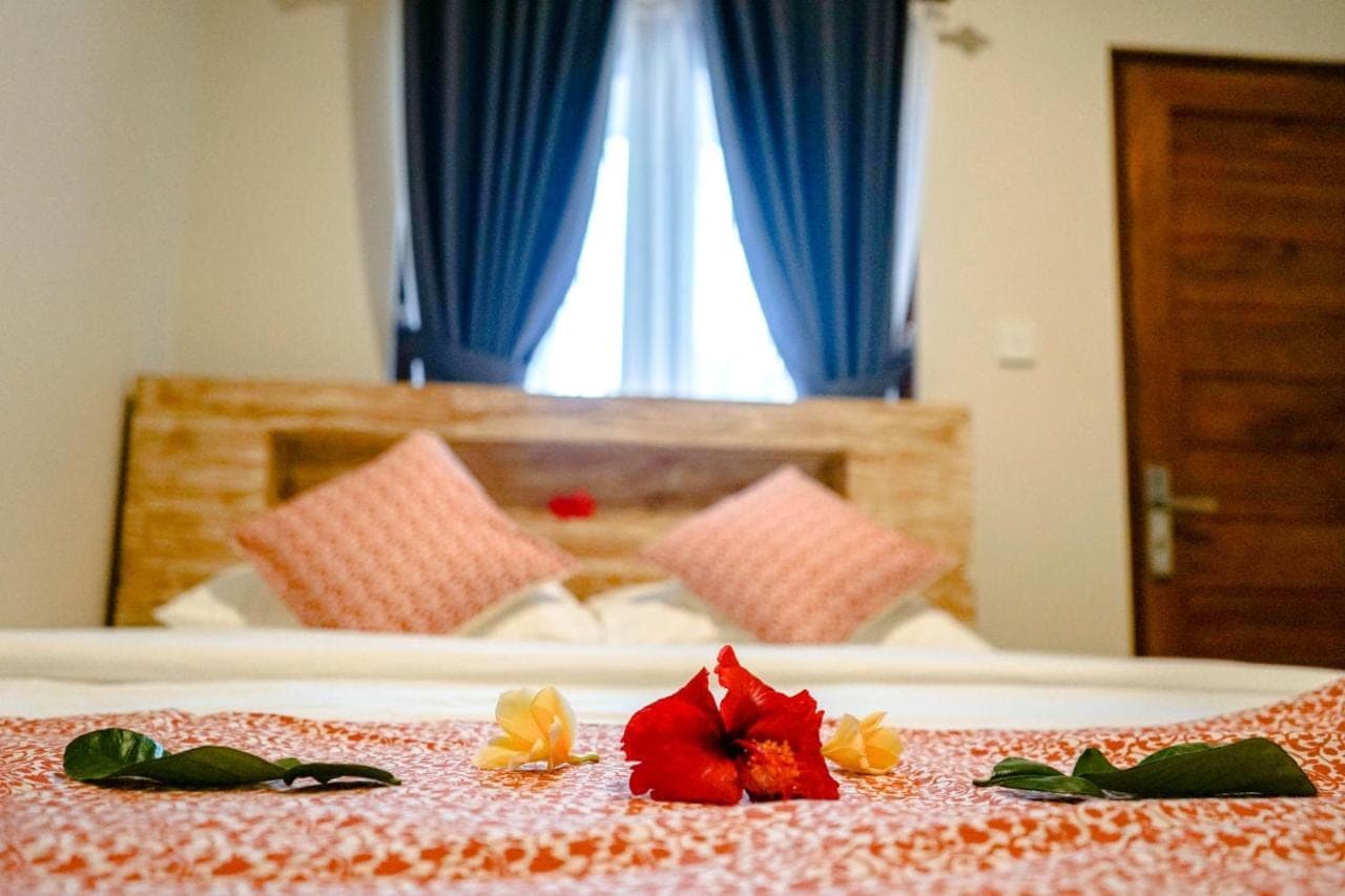 a bedroom with a bed with blue curtains and flowers on it at Adhi Homestay in Nusa Dua