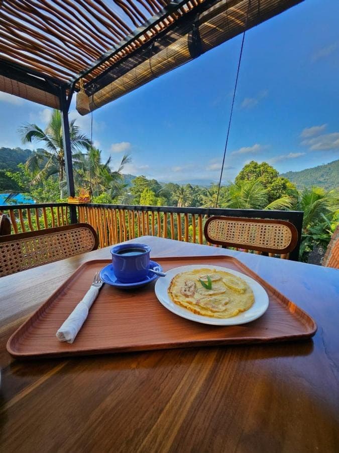 a table with a plate of food on a wooden table at Kubu Dangin Ogang Guest House in Sidemen