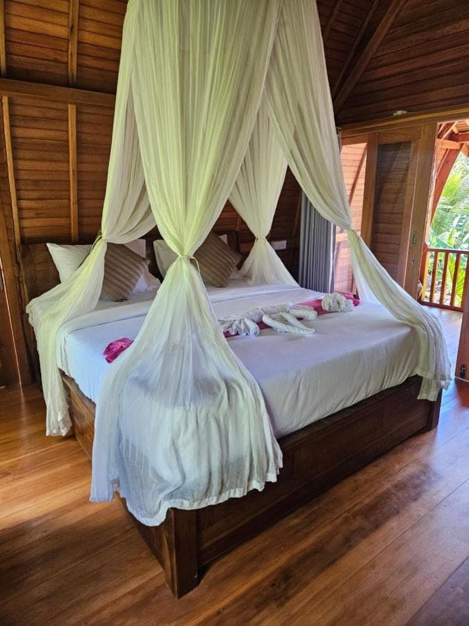 a bedroom with a bed with white drapes at Kubu Dangin Ogang Guest House in Sidemen