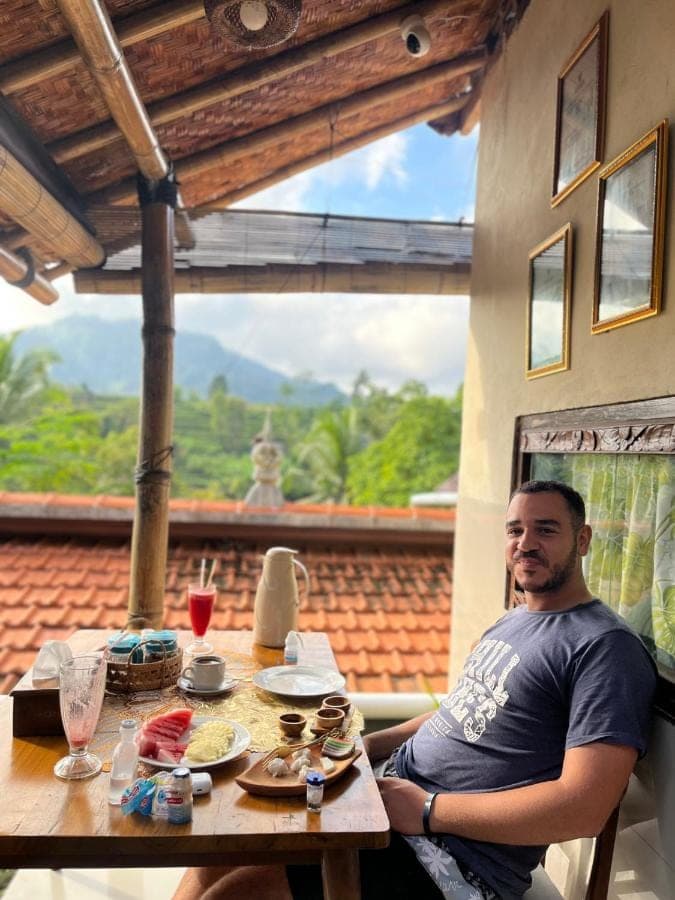 a man sitting at a table with food on it at Wayan Bola Homestay in Sidemen