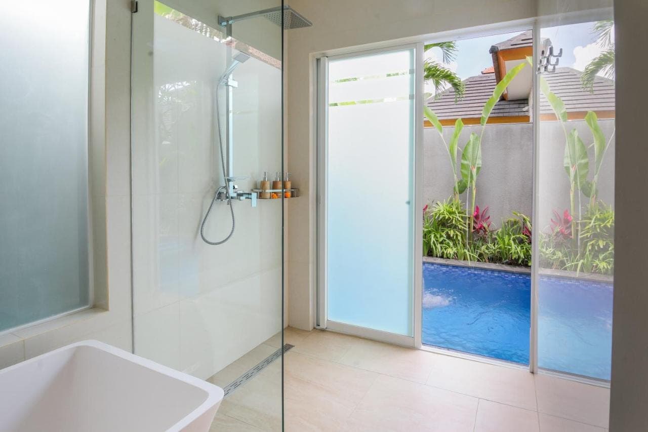 a bathroom with a shower with a swimming pool through a glass door at Le Cielo Romantic Villas by Maviba in Seminyak