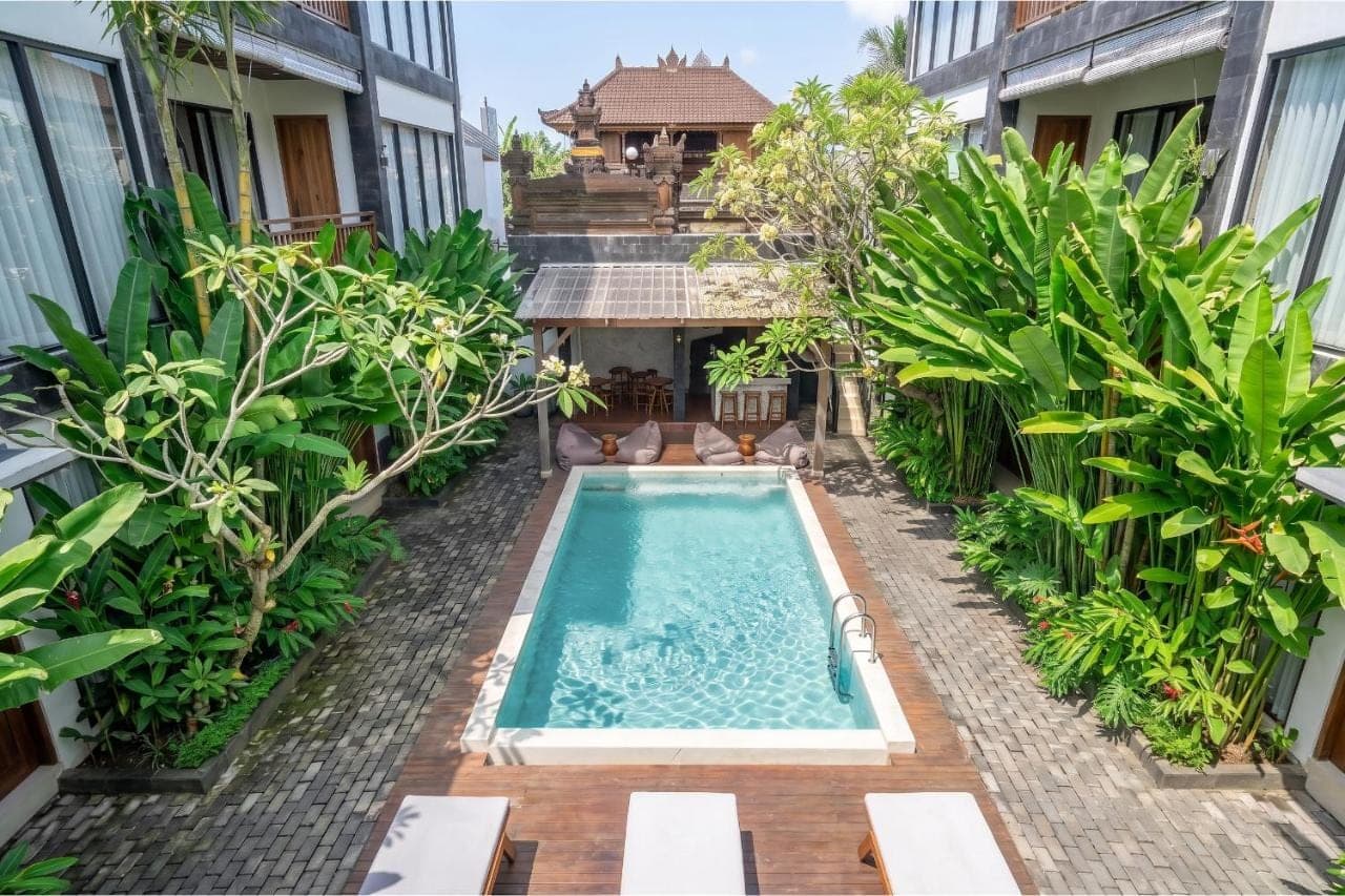 an outdoor swimming pool in a courtyard with plants at Sebelas Apartments by EVDEkimi - Modern Stay with Pool near Dining & Shops in Ubud