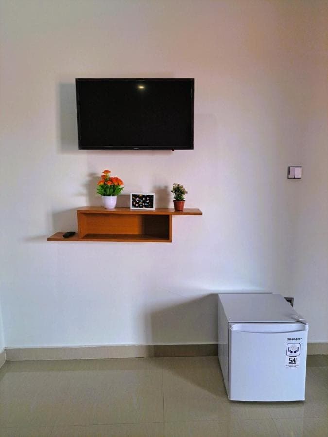 a flat screen tv on a white wall with two plants at Wayan House Seminyak in Seminyak