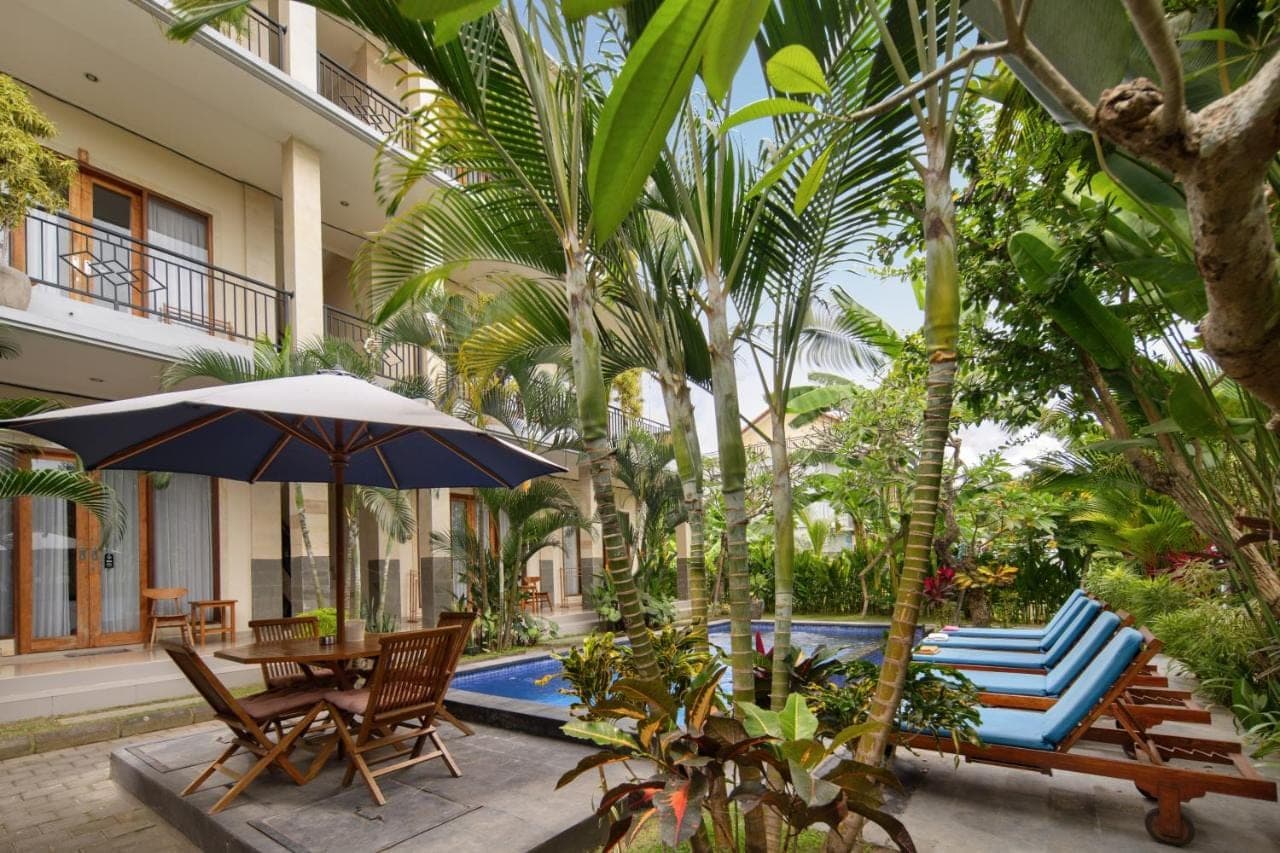 an outdoor patio with chairs and an umbrella and a pool at Canggu Nadi 2 Guest House in Canggu
