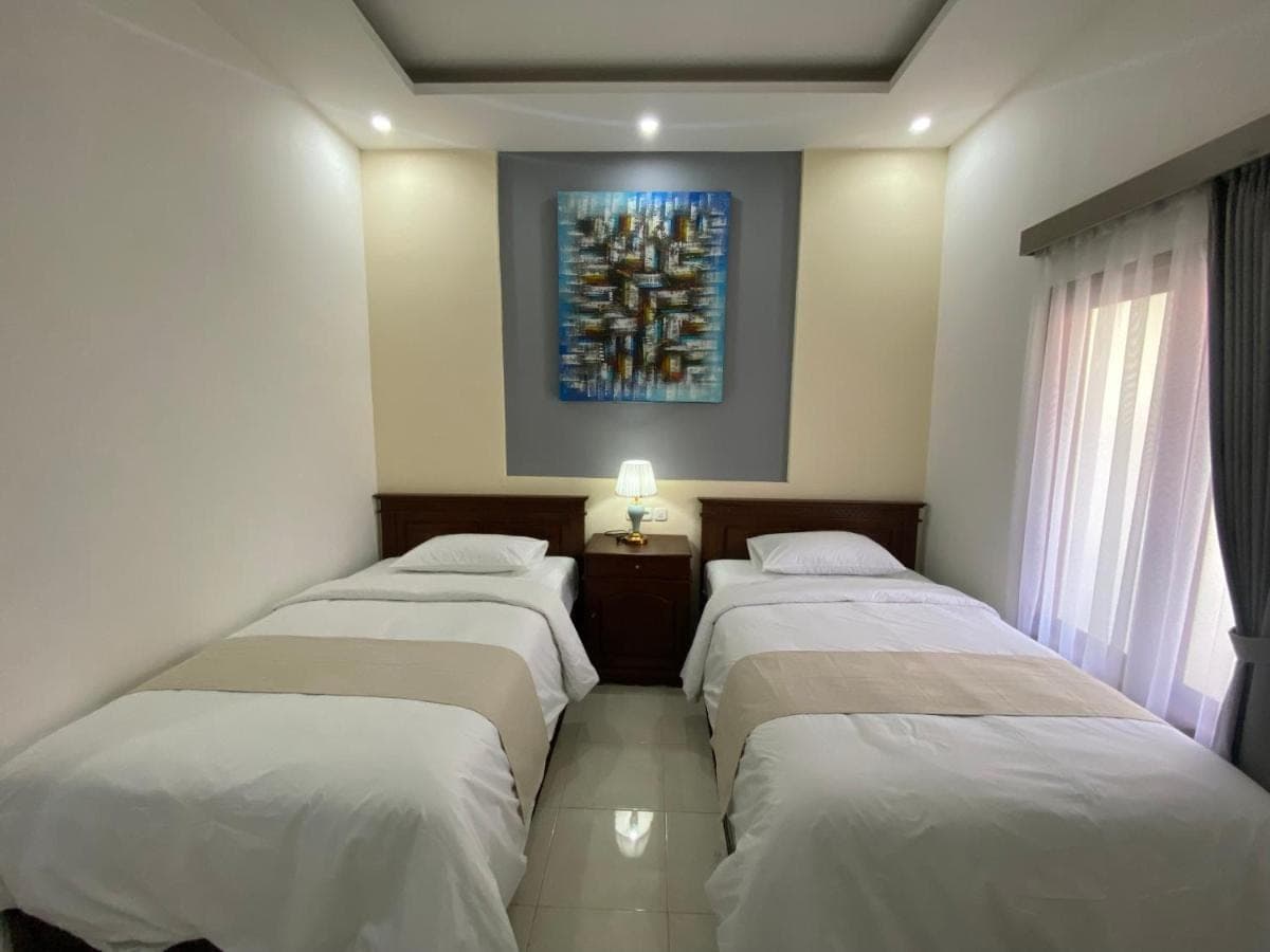three beds in a room with a painting on the wall at Bidadari Homestay Nusa Dua in Nusa Dua
