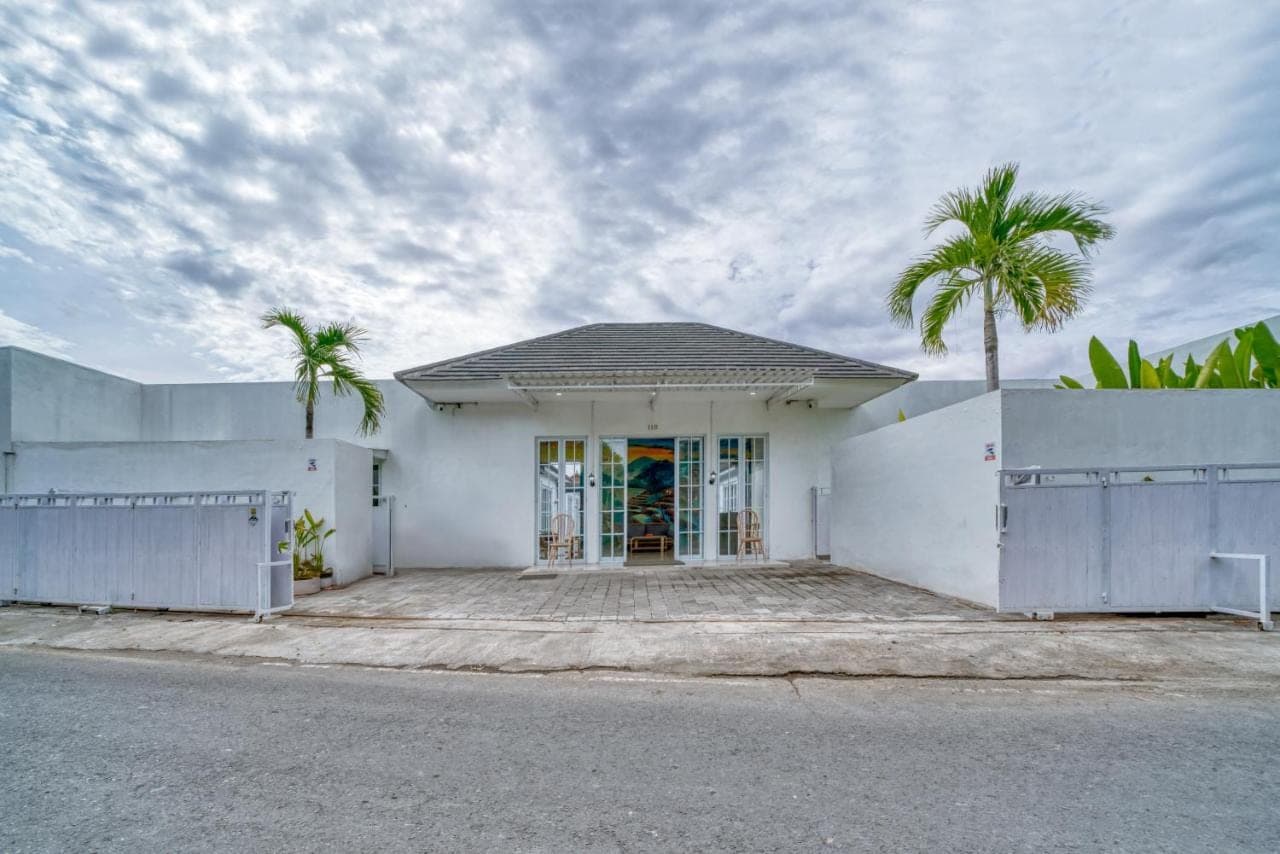 a white house with palm trees in front of it at 3BD Modern Apartment in Sanur with BBQ & huge shared pool in Sanur