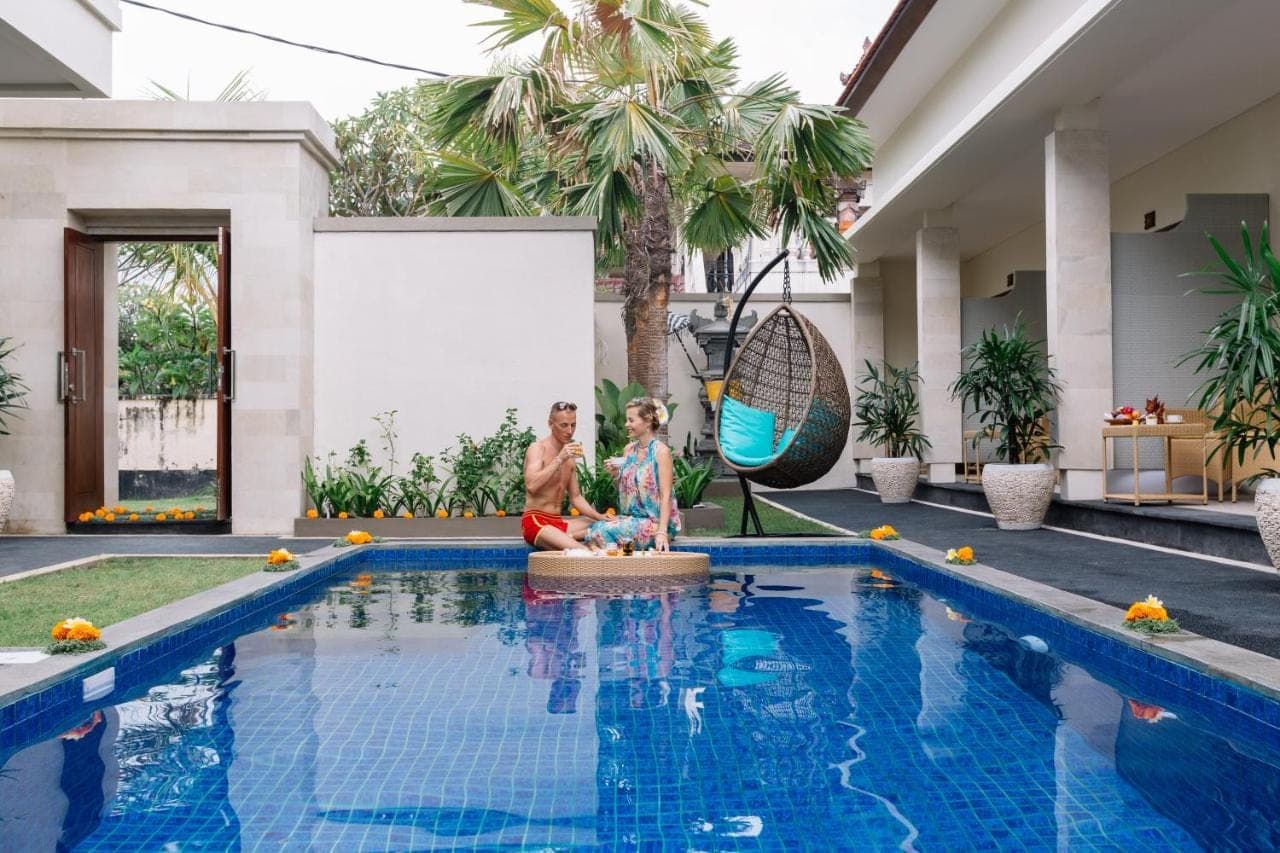 two people sitting next to a swimming pool at Kubu Benoa Guest House in Nusa Dua