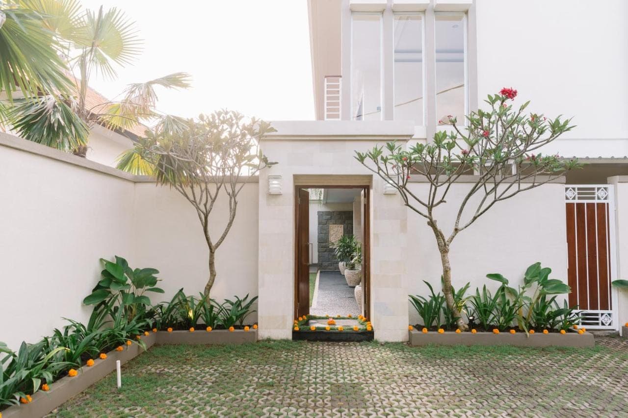 a white house with a door and trees at Kubu Benoa Guest House in Nusa Dua
