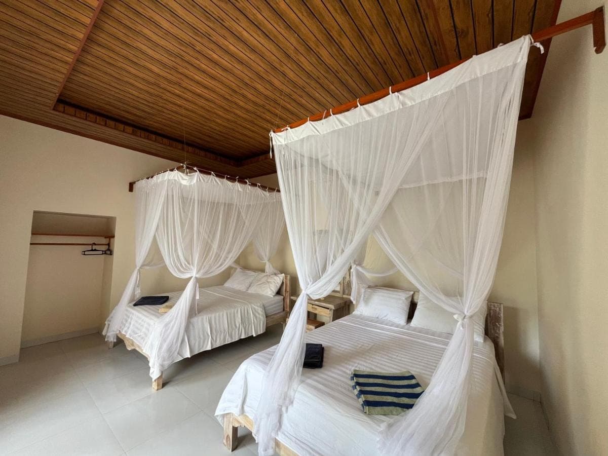 two beds in a room with white drapes at Ganesha Amed in Amed