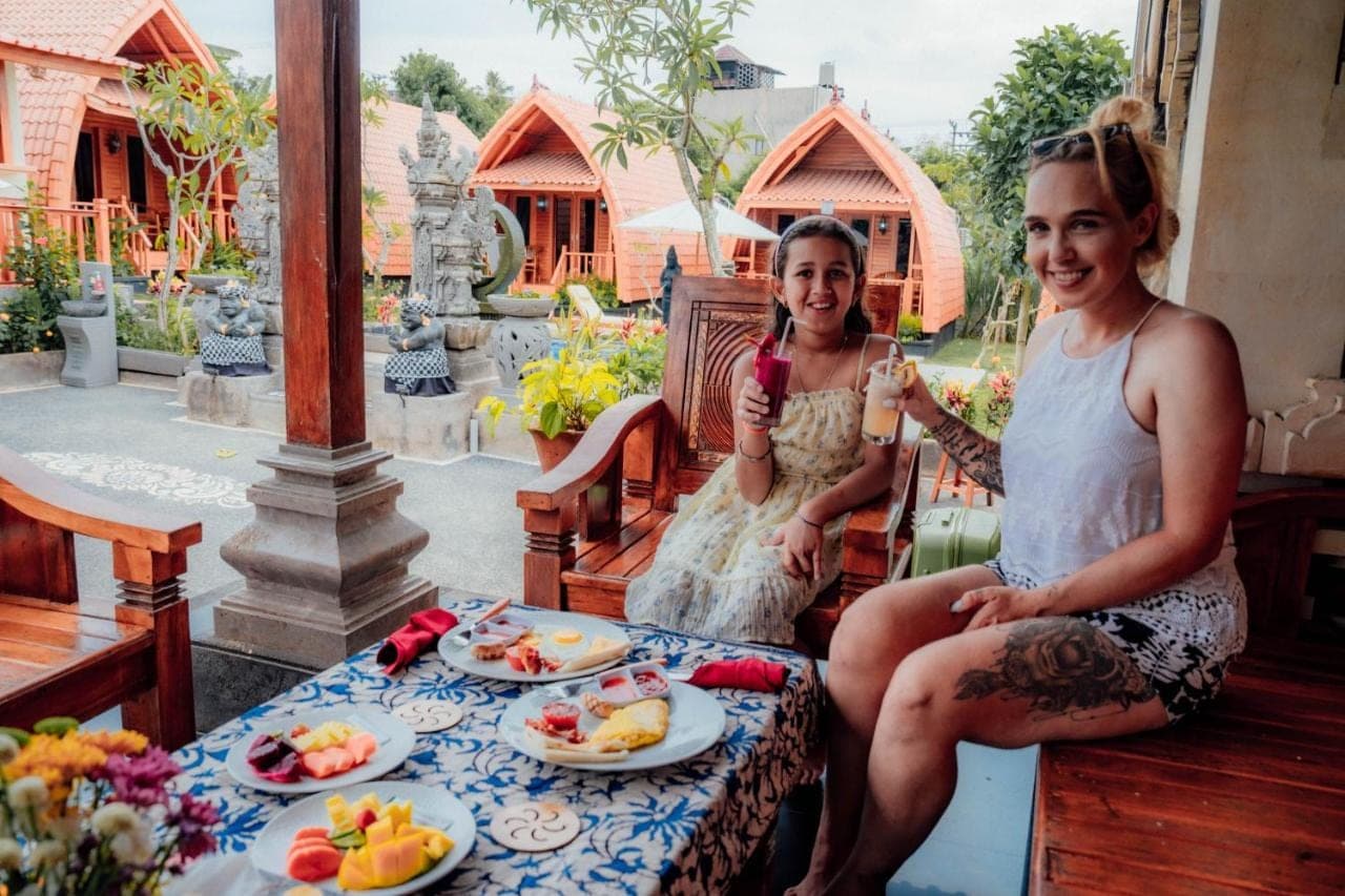 two women sitting on a porch with plates of food at Nusa Dua Huts Pondok Gajah Para by EPS in Nusa Dua