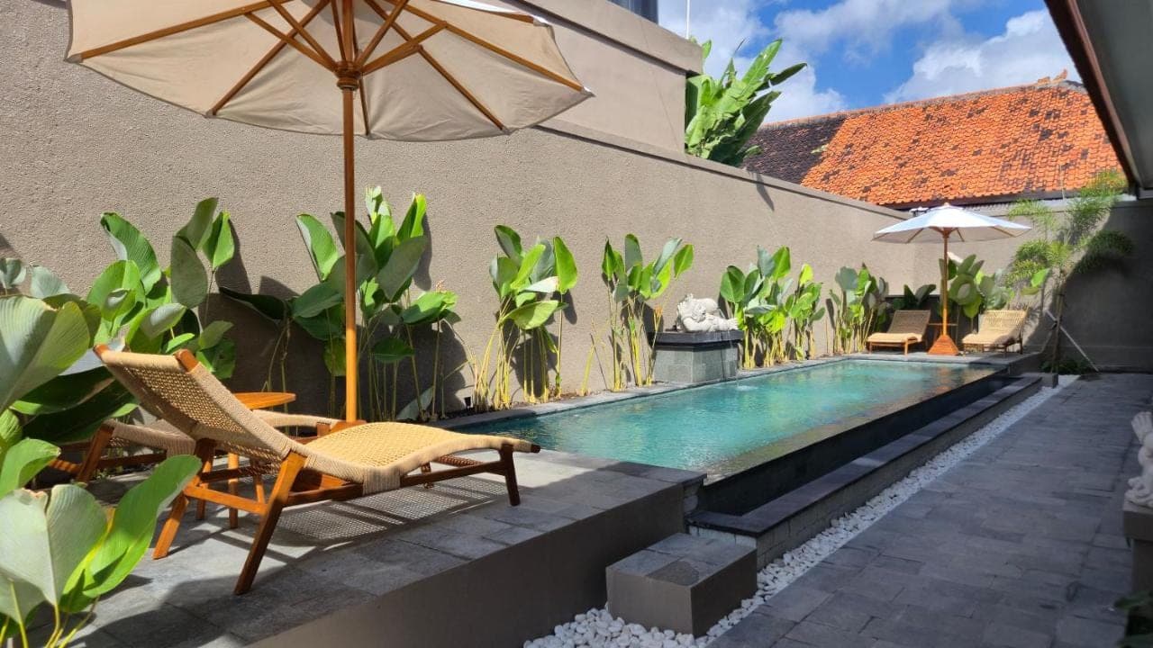 a swimming pool with two chairs and an umbrella at Kawitris Hidden Homestay in Nusa Dua