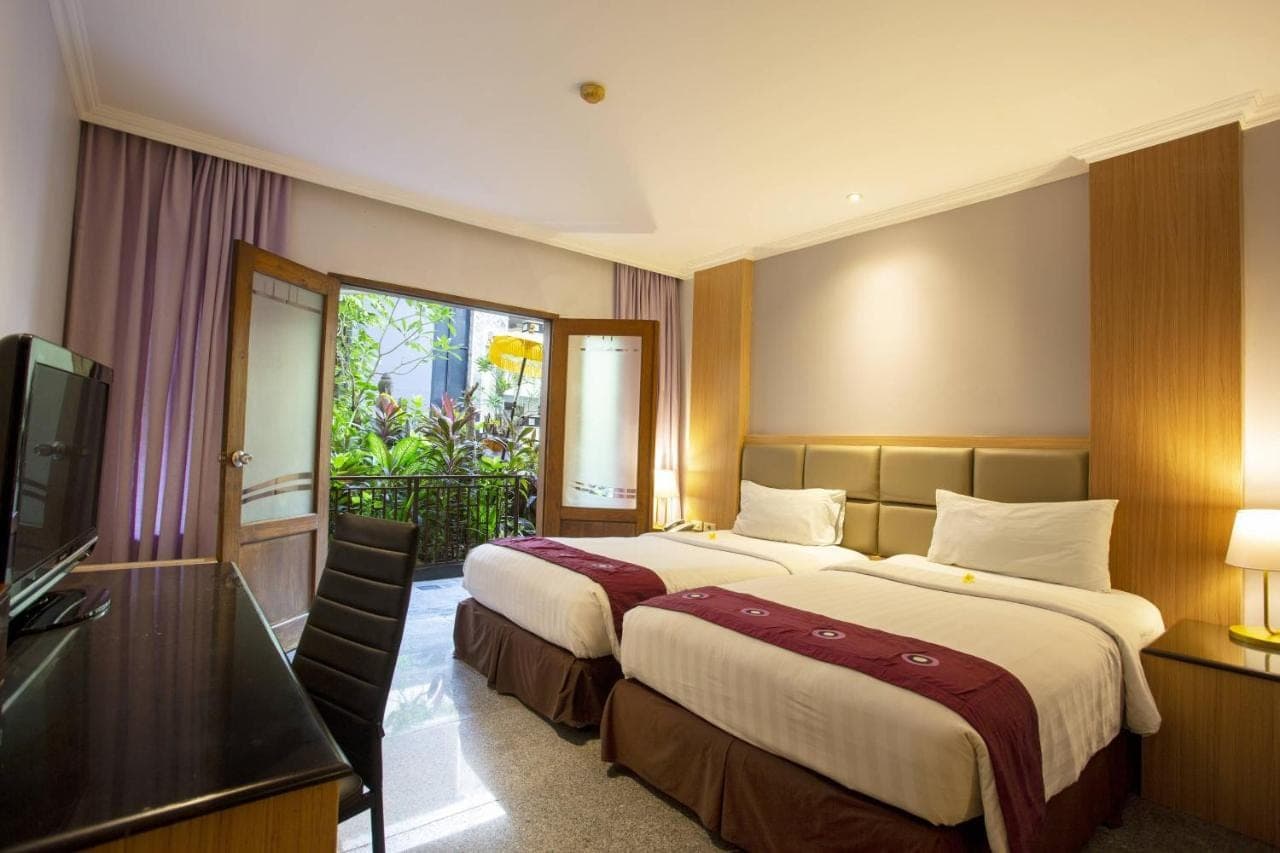 a hotel room with two beds and a television at Famous Hotel Kuta Formerly Permata Kuta Hotel in Kuta