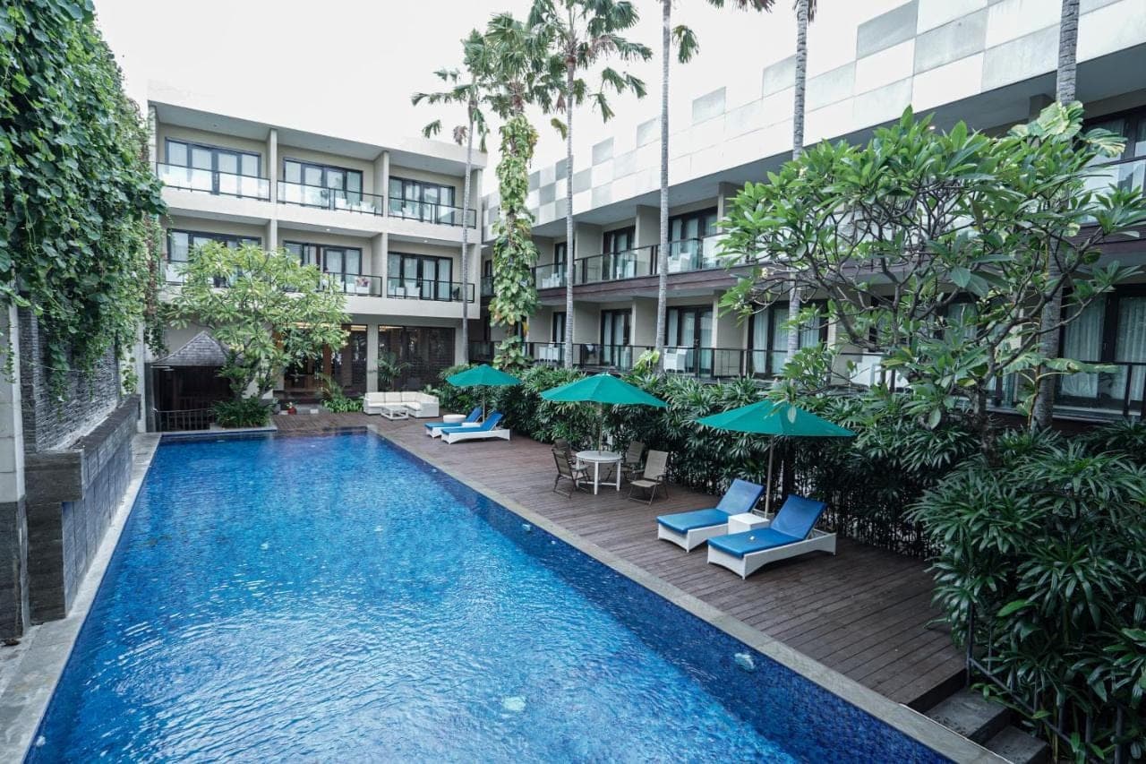 a swimming pool with chairs and umbrellas in front of a building at Dekuta in Kuta