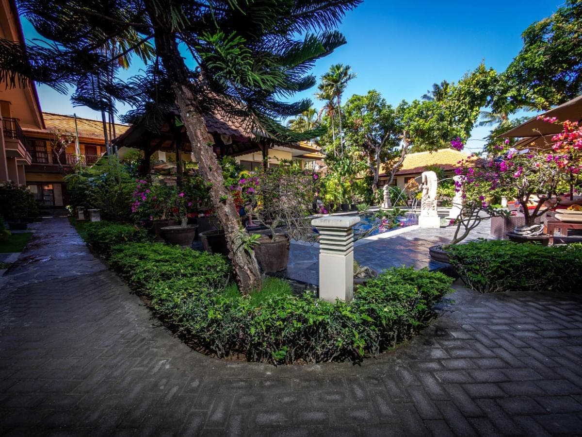 a courtyard with a tree and flowers and a fountain at Yulia Beach Inn Kuta in Kuta