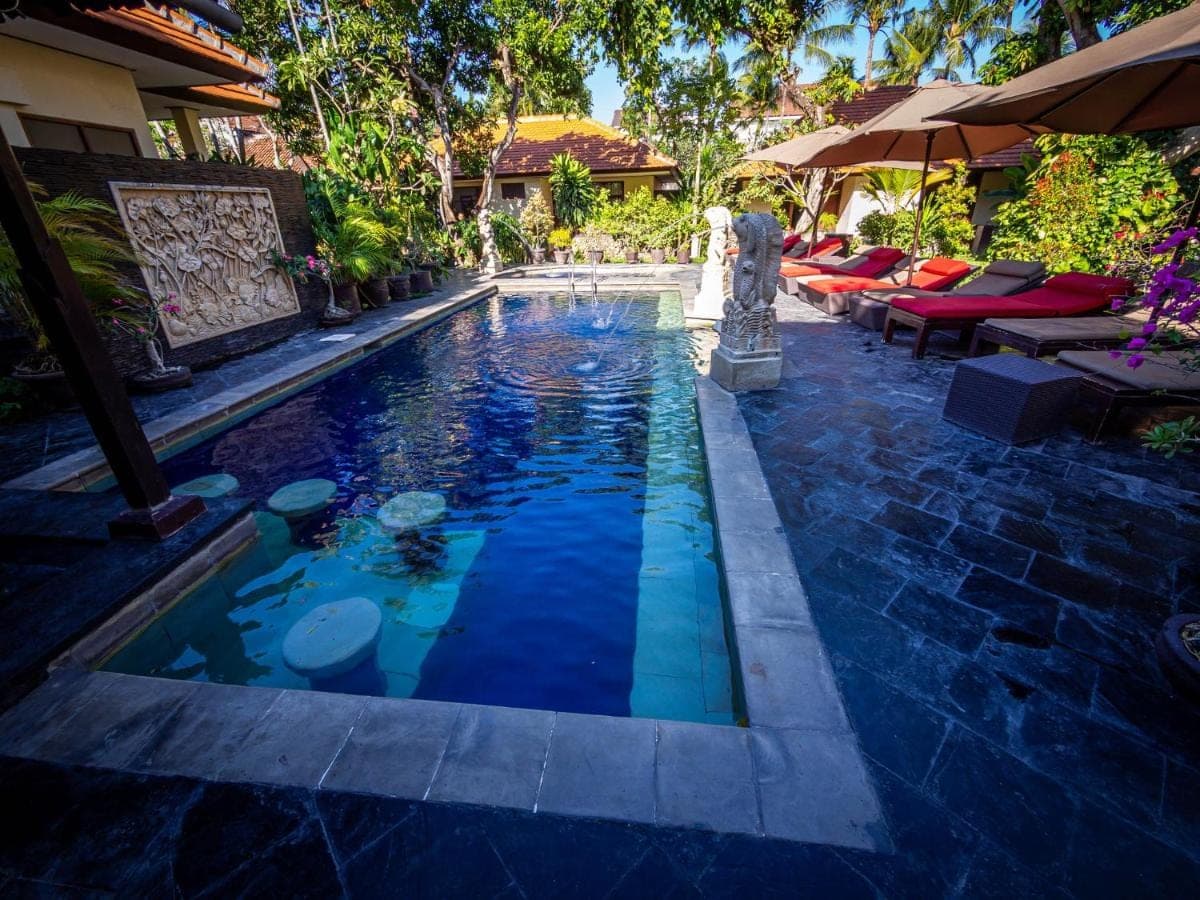 a swimming pool in a yard with some tables and umbrellas at Yulia Beach Inn Kuta in Kuta
