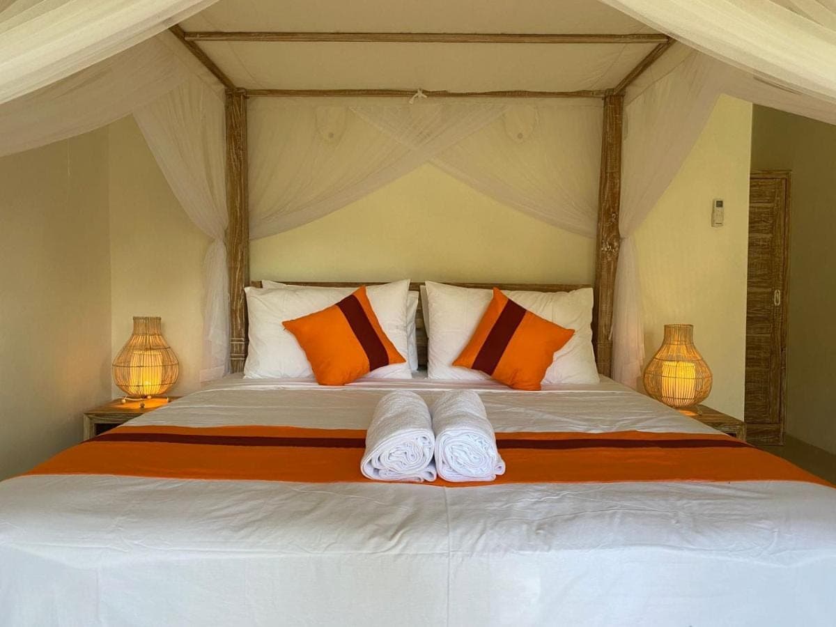 a bedroom with a bed with orange and white pillows at Comeon Amed in Amed