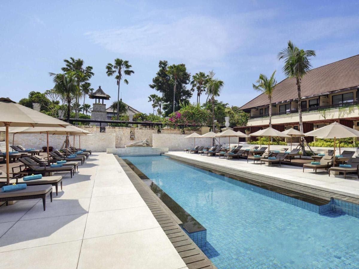 a pool at a resort with lounge chairs and umbrellas at Novotel Bali Benoa in Nusa Dua