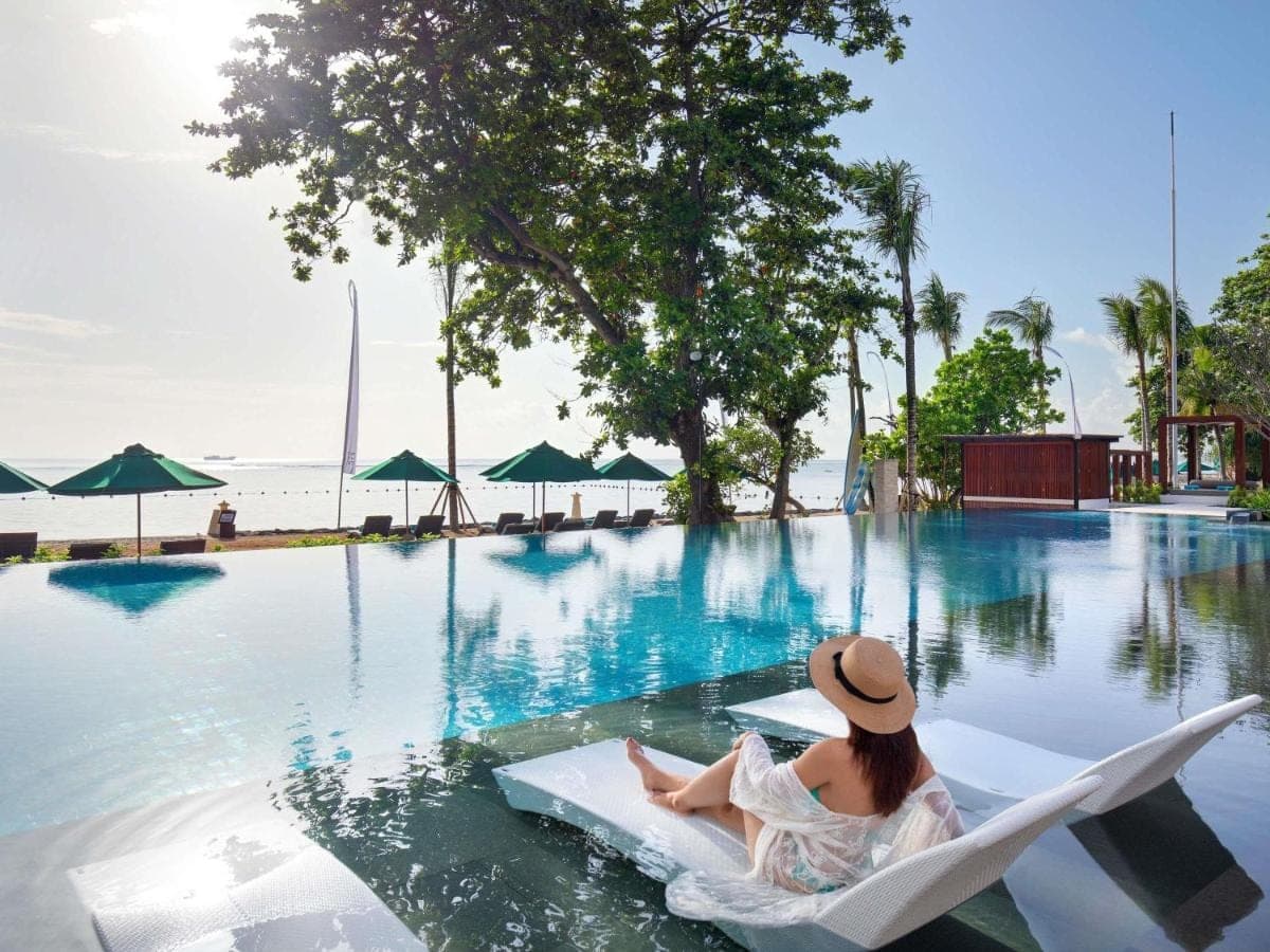 a woman sitting in a chair next to a swimming pool at Novotel Bali Benoa in Nusa Dua