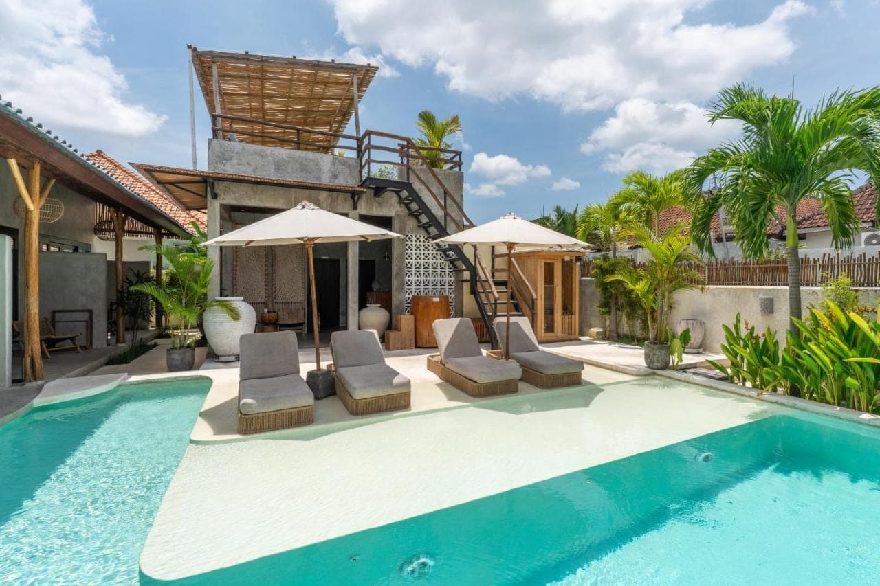 a swimming pool with chairs and umbrellas next to a house at Kano Twin in Canggu