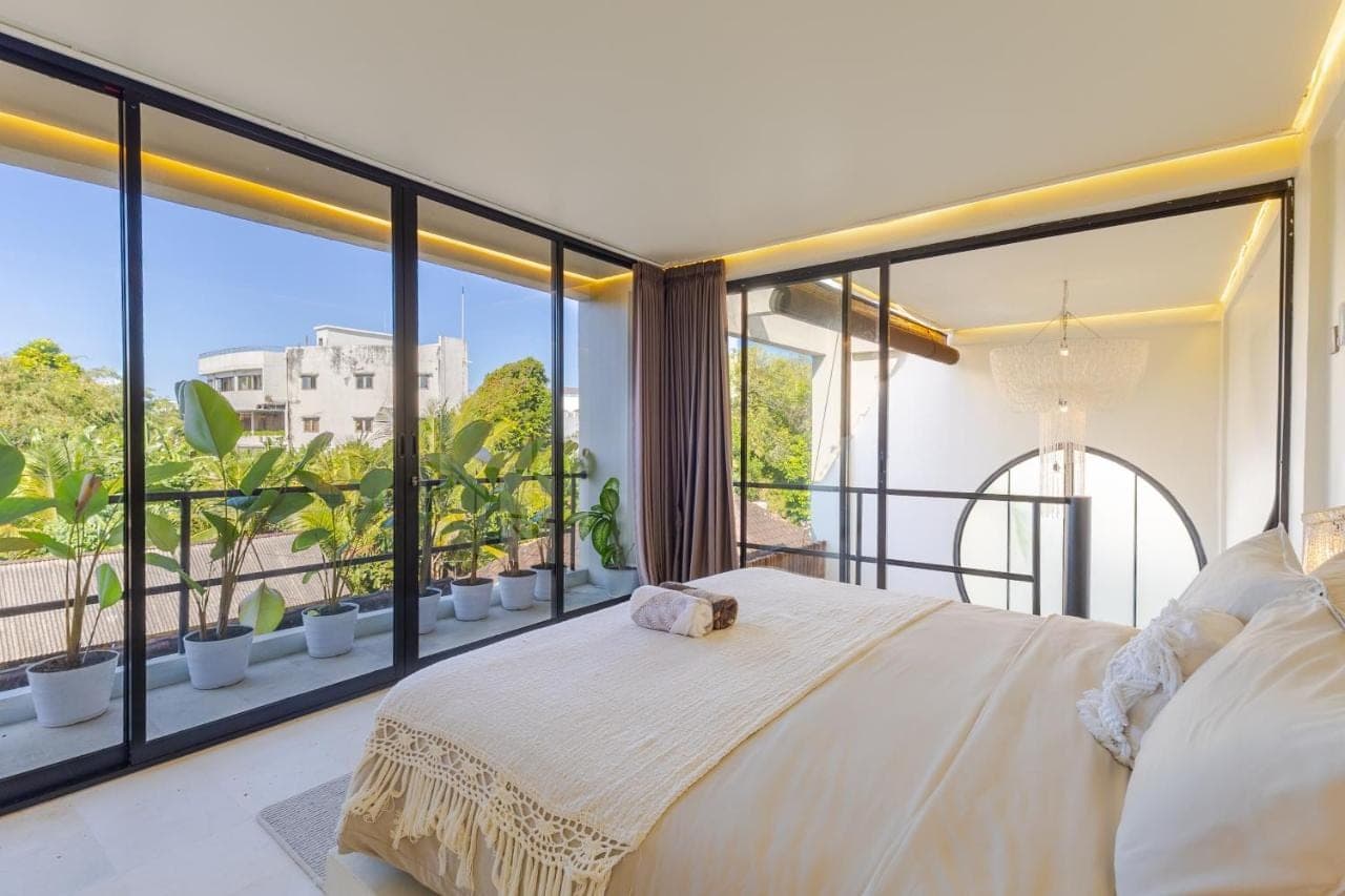 a bedroom with a bed and large windows at Djati Retreat & Yoga Lounge by Pertama Stay in Nusa Dua