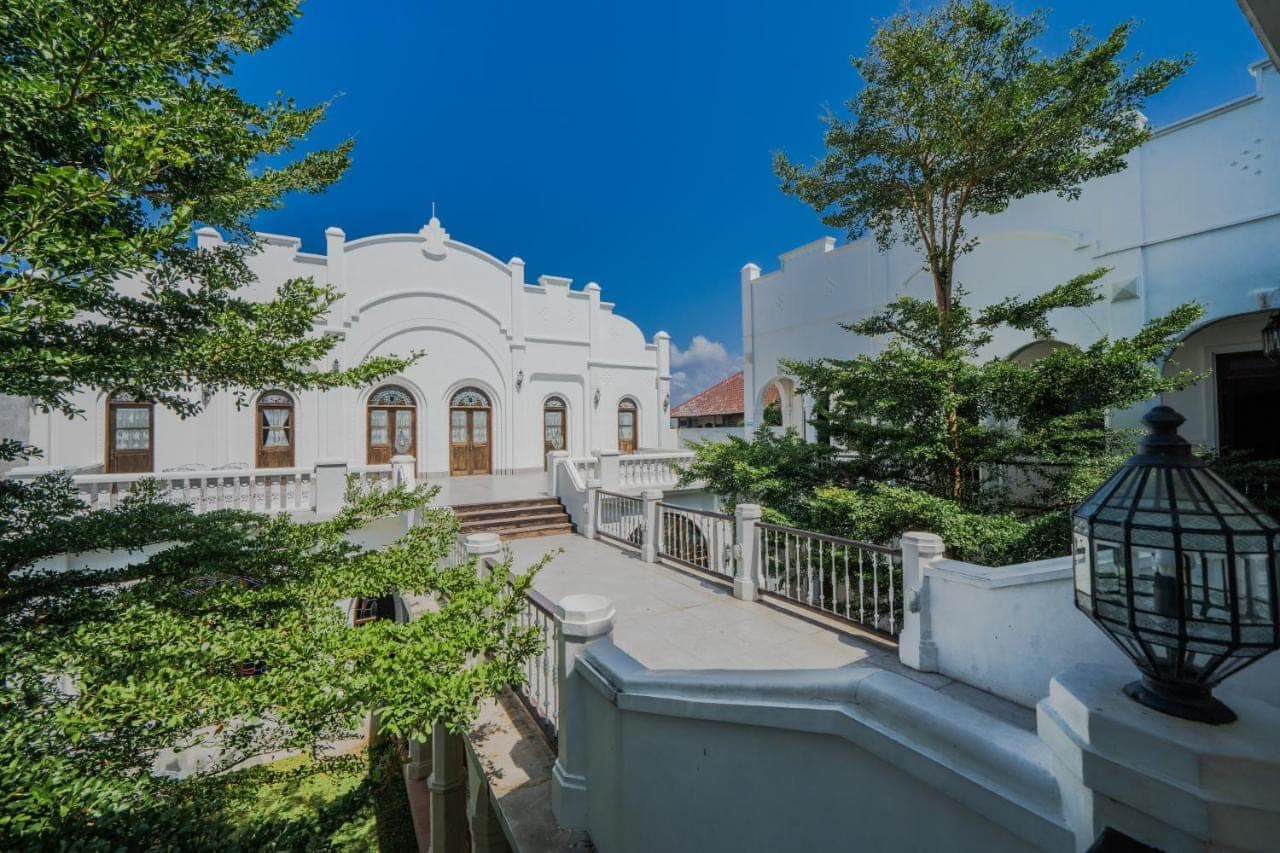 a white house with a staircase and trees at Pitaloka Hotel Sanur By DeWizZ Management in Sanur